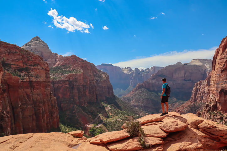 A hiker standing on a red rock cliff overlooking Zion Canyon